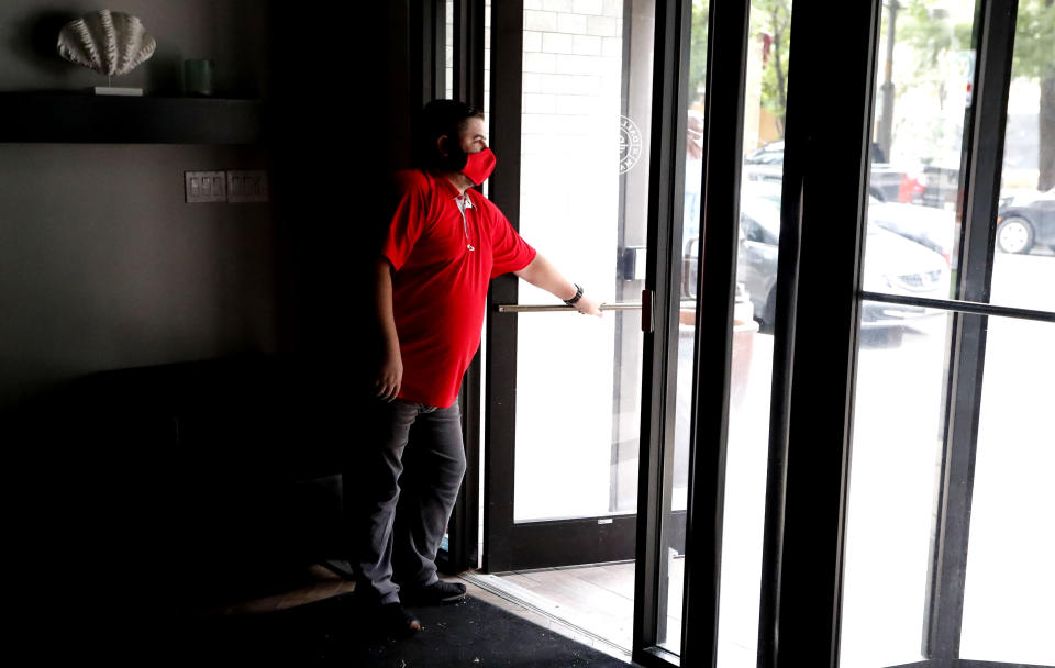 Wearing a mask amid concerns of the spread of the coronavirus, Dimitris Anagnostis opens the door to Chop House Burgers before the restaurant opened in downtown Dallas, Wednesday, July 8, 2020. (AP Photo/LM Otero)