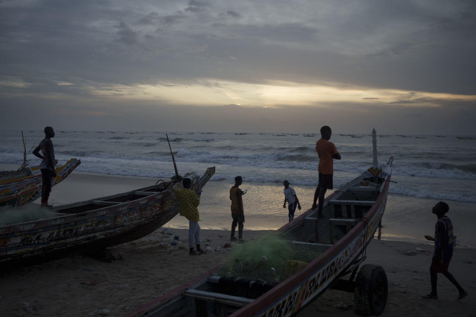 Senegalese youth gather around pirogues on the beach at dusk in Fass Boye, Senegal, Tuesday, Aug. 29, 2023. (AP Photo/Felipe Dana)