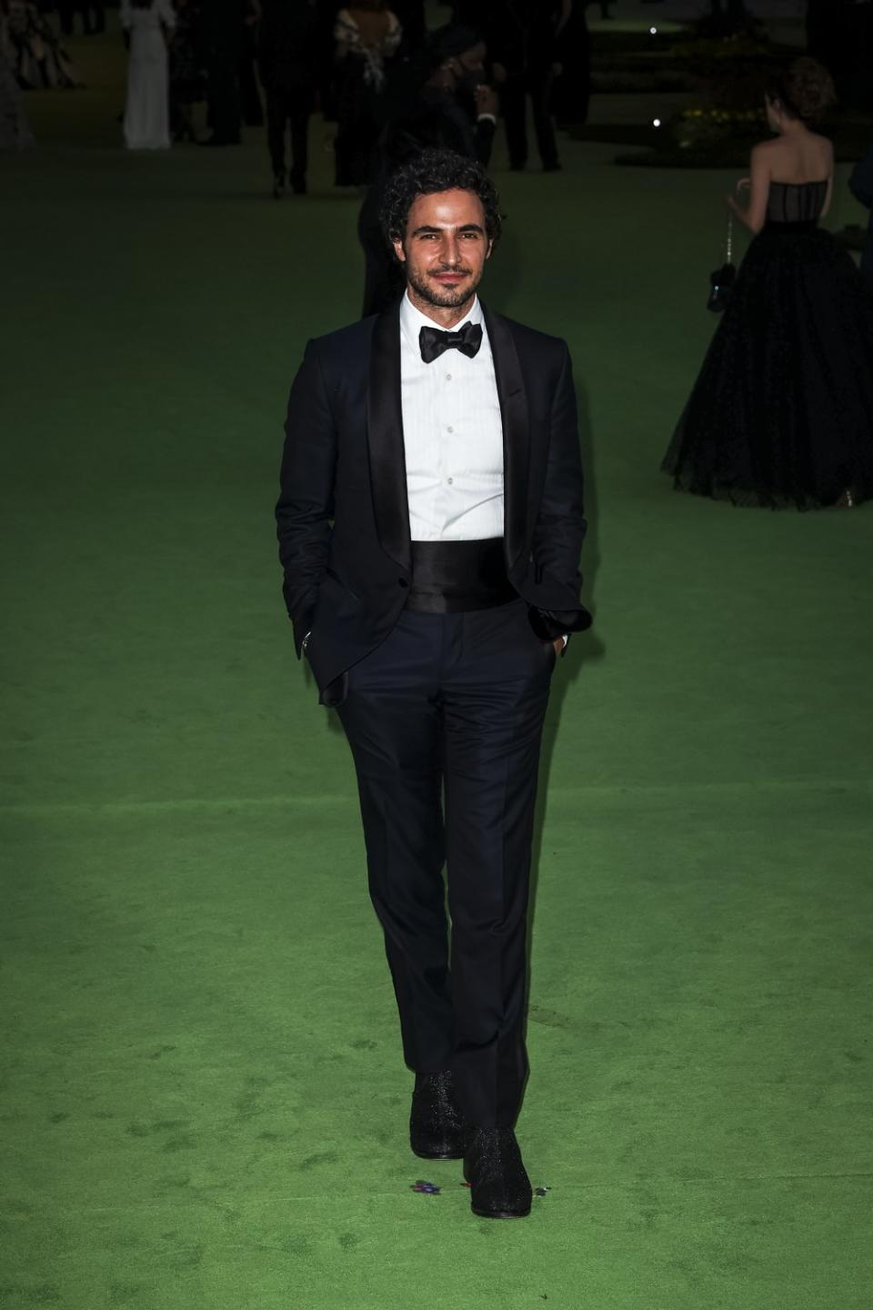 A man in a black tuxedo posing on a green carpet