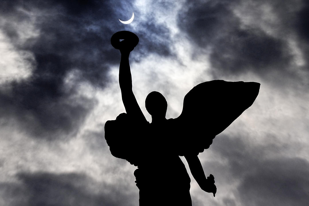 The moon makes its way in front of the sun during a total solar eclipse framed above the angel atop the Princes' Gates, in Toronto, Monday, April 8, 2024. THE CANADIAN PRESS/Frank Gunn