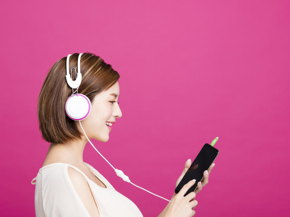 A young woman wears headphones connected to her smartphone.