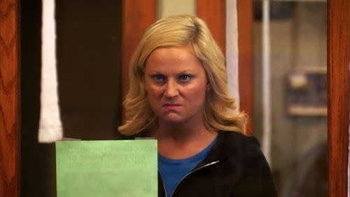 Character Leslie Knope from Parks and Recreation looks displeased while holding a document