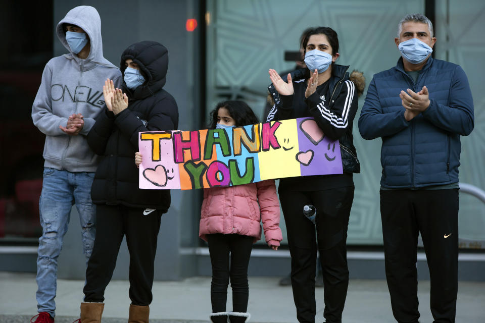 A family holds a sign and applauds healthcare workers outside St. Paul's Hospital, as a convoy of first responders with lights and sirens activated parade past to show support for the hospital staff, in Vancouver, British Columbia, Sunday, April 5, 2020. (Darryl Dyck/The Canadian Press via AP)