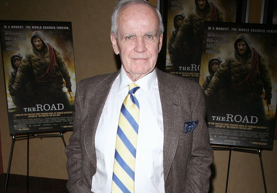 Author Cormac McCarthy standing in front of movie posters for The Road