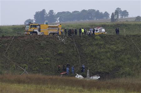 Investigators and firefighters stand in front of a wreckage of a twin propeller airplane at South Africa's Lanseria airport outside Johannesburg February 3,2014. REUTERS/Siphiwe Sibeko