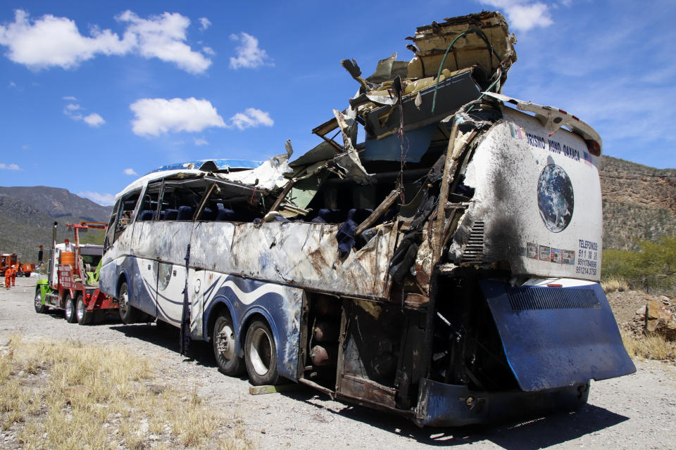 A crashed bus sits attached to a tow truck the side of the road near Villa de Tepelmeme, Oaxaca state, Mexico, Friday, Oct. 6, 2023. At least 18 migrants from Venezuela and Peru died early Friday in the bus crash, authorities said. (AP Photo/Nemesio Mendez Jiménez)