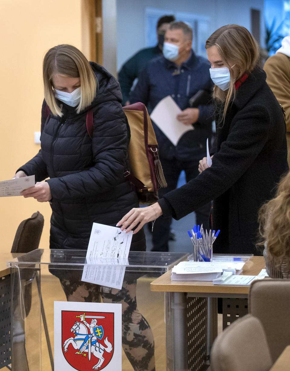 People wearing face masks to protect against coronavirus, vote at a polling station during early voting in the second round of a parliamentary election in Vilnius, Lithuania, Thursday, Oct. 22, 2020. Lithuanians are voting in the second round of a parliamentary election on upcoming Sunday during the rise in the incidence of coronavirus infection in the country. (AP Photo / Mindaugas Kulbis)