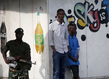 Young men stand next to a soldier during a protest against Burundi President Pierre Nkurunziza and his bid for a third term in Bujumbura, Burundi, May 18, 2015. REUTERS/Goran Tomasevic