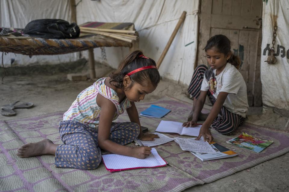 Garima, 10, right, and her sister Arima, 7, left, study outside their restored home on the flood plain of Yamuna River after coming from school in New Delhi, India, Friday, Sept. 29, 2023. Their family were among the hundreds that were displaced by the recent floods in the Indian capital's Yamuna River. (AP Photo/Altaf Qadri)