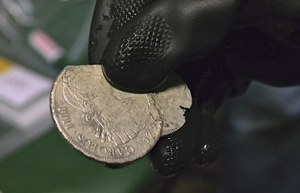 In this undated photo made available by the Spain's Culture Ministry, a member of the Ministry technical crew displays two of the 594,000 coins and other artifacts found in the Nuestra Senora de las Mercedes, a Spanish galleon sunk by British warships in the Atlantic while sailing back from South America in 1804, in a warehouse in Tampa, Fla. A 17-ton trove of silver coins recovered from the Spanish galleon was set to be flown Friday Feb. 24, 2012 from the United States to Spain, concluding a nearly five-year legal struggle with Odyssey Marine Exploration, the Florida deep-sea explorers who found and recovered it. (AP Photo/Spain's Culture Ministry, HO)