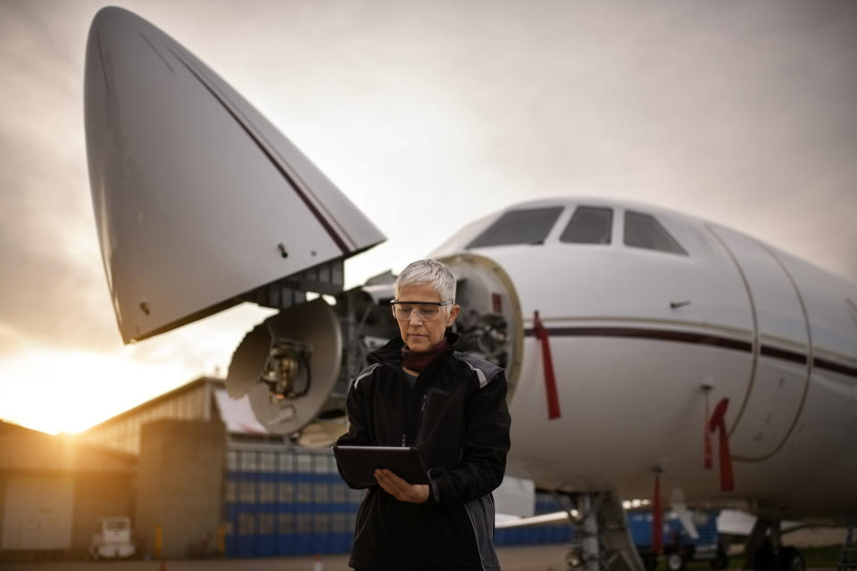 A female aviation worker checks her tablet as she stands by a plane