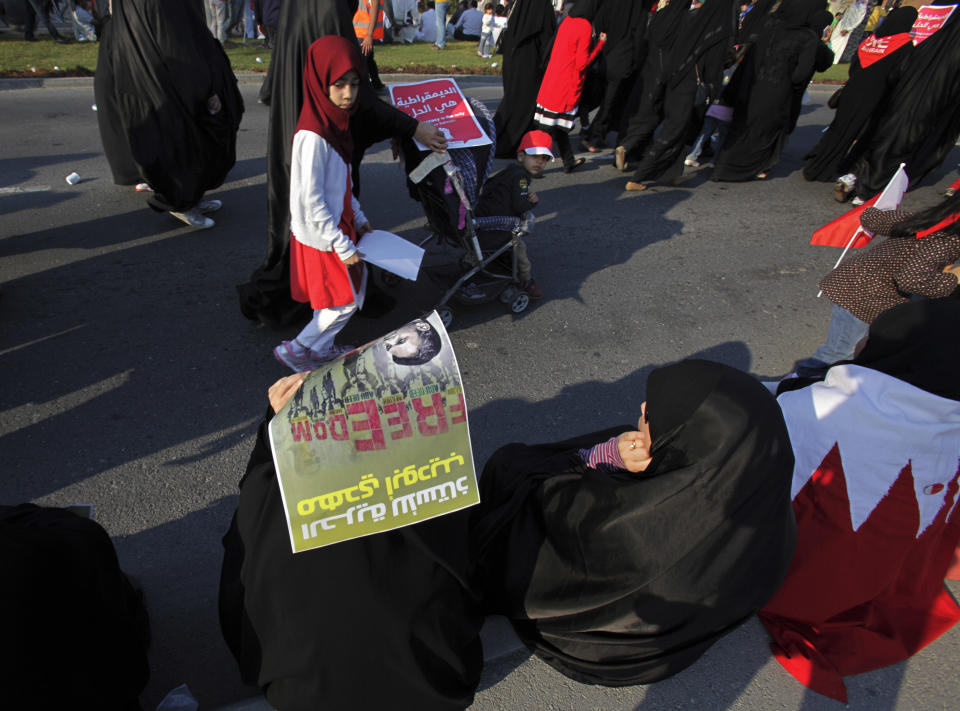 Bahraini women and children walk to join a pro-democracy march near Diraz, west of the capital of Manama, Bahrain, Saturday, Feb. 15, 2014. Tens of thousands of protesters marched down a divided four-lane highway, calling for the long-serving prime minister, Sheik Khalifa bin Salman Al Khalifa, to step down and for democracy in the Gulf island kingdom. The lower sign reads, "freedom for teacher Mahdi Abu Deeb," referring to the jailed leader of the teachers' union. Arabic on the red sign reads, "democracy is the solution." (AP Photo/Hasan Jamali)