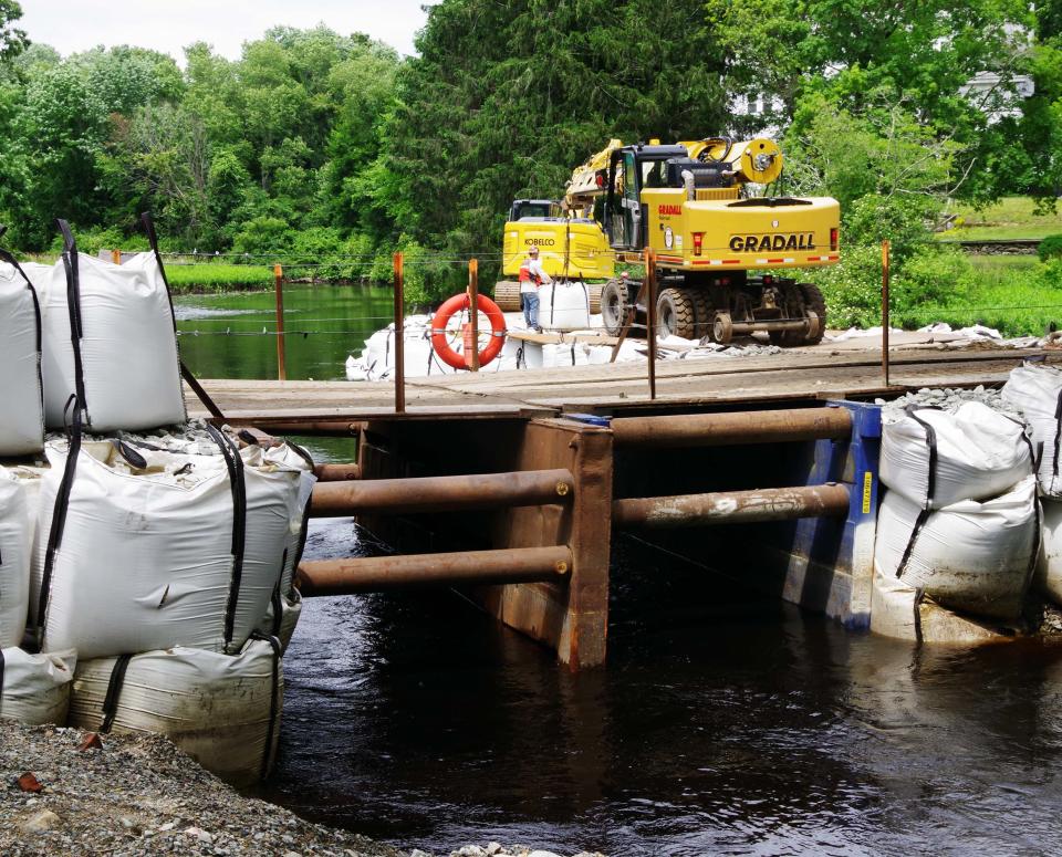 A temporary bridge is built in the area of the High Street dam bridge in Bridgewater to allow for placement of sandbags to control water flow as crews build a new bridge. Two cranes work together to deliver and place heavy duty sandbags in an effort to control water flow near the bridge. On Tuesday, June 27, 2023, more bags are added to secure the structure.