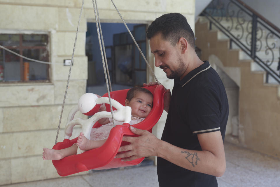 Khalil al-Sawadi plays with his adopted daughter Afraa in Jinderis, Syria, on Saturday, Aug. 5, 2023. Afraa was born under the rubble of her family home, destroyed by the deadly earthquake that hit Turkey and Syria six months ago, killing her parents and siblings. (AP Photo/Ghaith Alsayed)