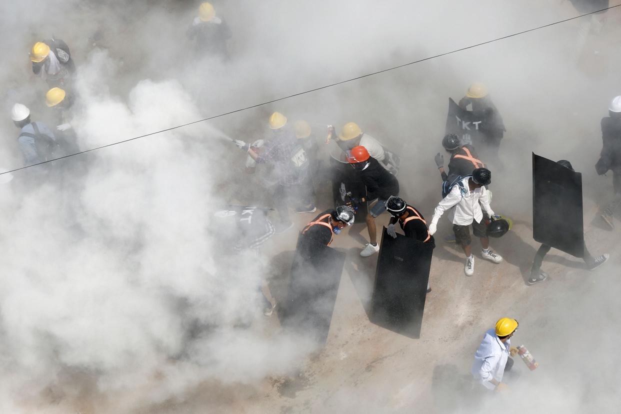 <p>Protesters react as they are engulfed by tear gas fired in Yangon </p> (AFP)