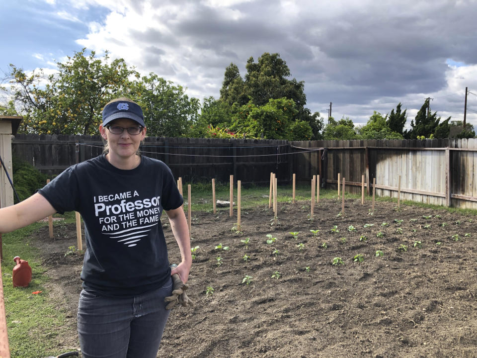 In this March 23, 2020 photo, Lindsay Waldrop stands near her garden at her home in Anaheim, Calif. Waldrop plowed 1,000 square feet of grass to start a garden this year. She has planted dozens of tomatoes, eggplants and peppers with many more crops started as seeds. As the arrival of spring in the Northern Hemisphere coincides with orders to stay at home and out of crowds, the backyard garden has become a getaway for the mind in chaotic times. (Matt Snyder via AP).