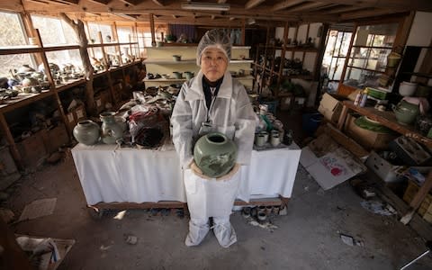 Ceramic artist Keiko Onoda holds up one of her husband Kanjiro's pottery works inside their atelier in Namie, The Onodas fled to Tokyo over radiation fears and have remained there since, occasionally returning to collect their belongings - Credit: Simon Townsley