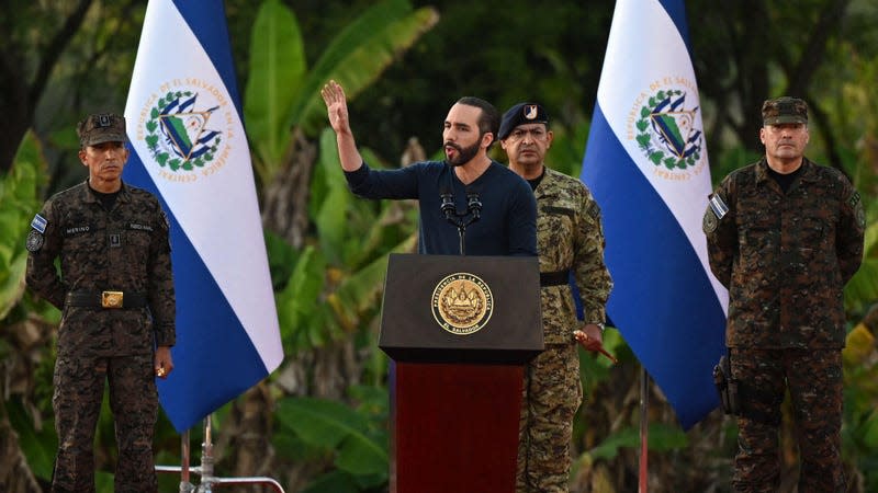 El Salvador President Nayib Bukele stands at a lectern surrounded by El Salvador flags and military personnel.