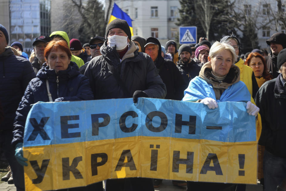 People hold a Ukrainian flag with a sign that reads: "Kherson is Ukraine", during a rally against the Russian occupation in Kherson, Ukraine, Sunday, March 20, 2022. Ever since Russian forces took the southern Ukrainian city of Kherson in early March, residents sensed the occupiers had a special plan for their town. Now, amid a crescendo of warnings from Ukraine that Russia plans to stage a sham referendum to transform the territory into a pro-Moscow "people's republic," it appears locals guessed right. (AP Photo/Olexandr Chornyi)