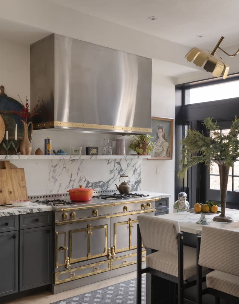 Kitchen with gold-trimmed oven with large oven hood and marble backsplash.