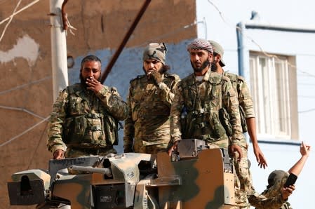 Members of Syrian National Army, known as Free Syrian Army, stand on top of an armored vehicle in the Turkish border town of Ceylanpinar