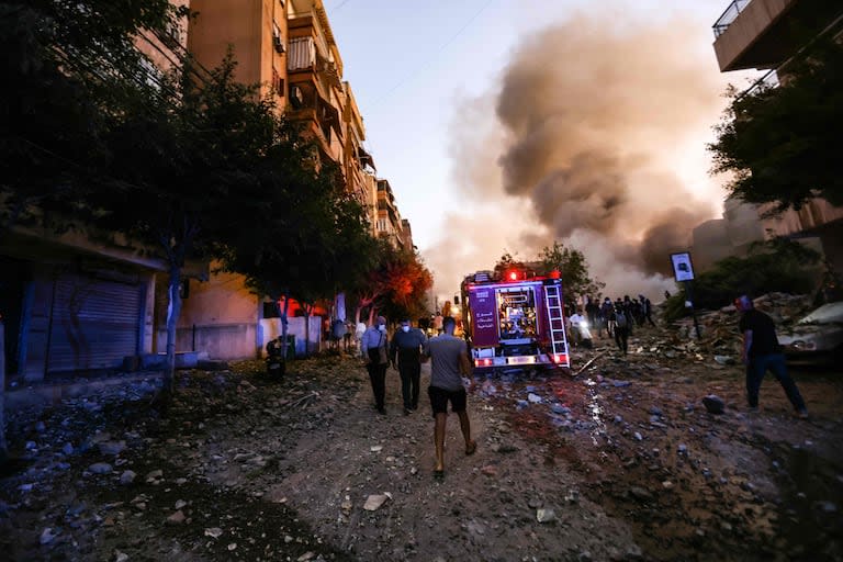 Personas y un camión de bomberos corren hacia el lugar de un ataque aéreo israelí en el barrio de Haret Hreik, en los suburbios del sur de Beirut, el 27 de septiembre de 2024. 