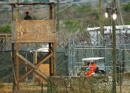 A Camp X-Ray detainee (R) is transported in an electric cart March 27, 2002 in Guantanamo Bay, Cuba. Over 300 detainees are being held at the camp as work continues on a more permanent prison nearby. (Photo by Chris Hondros/Getty Images)