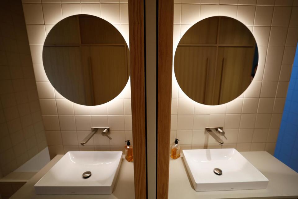 Light glows behind a mirror above a sink, reflected in a mirror.