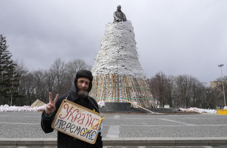 A man holds a poster reading "Ukraine will win" against the background of a monument of Taras Shevchenko, a famous Ukrainian poet and a national symbol, covered with bags to protect it from the Russian shelling in Kharkiv, Ukraine, Sunday, March 27, 2022. The bronze 16 meter high monument was opened in 1935, survived WWII and is considered one of the world's best monuments to Shevchenko. Kharkiv is Ukraine's second biggest city 30 kilometers of the Russian border. (AP Photo/Efrem Lukatsky)