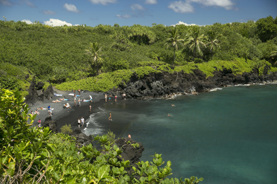 FILE - People spend time on the black sand beach at Waianapanapa State Park in Hana, Hawaii, on Sept. 24, 2014. Taking care of Hawaii's unique natural environment costs money and now the state wants tourists to help pay for it, especially because growing numbers are traveling to the islands to enjoy the beauty of its outdoors — including some lured by dramatic vistas they've seen on social media. (AP Photo/Marco Garcia, File)