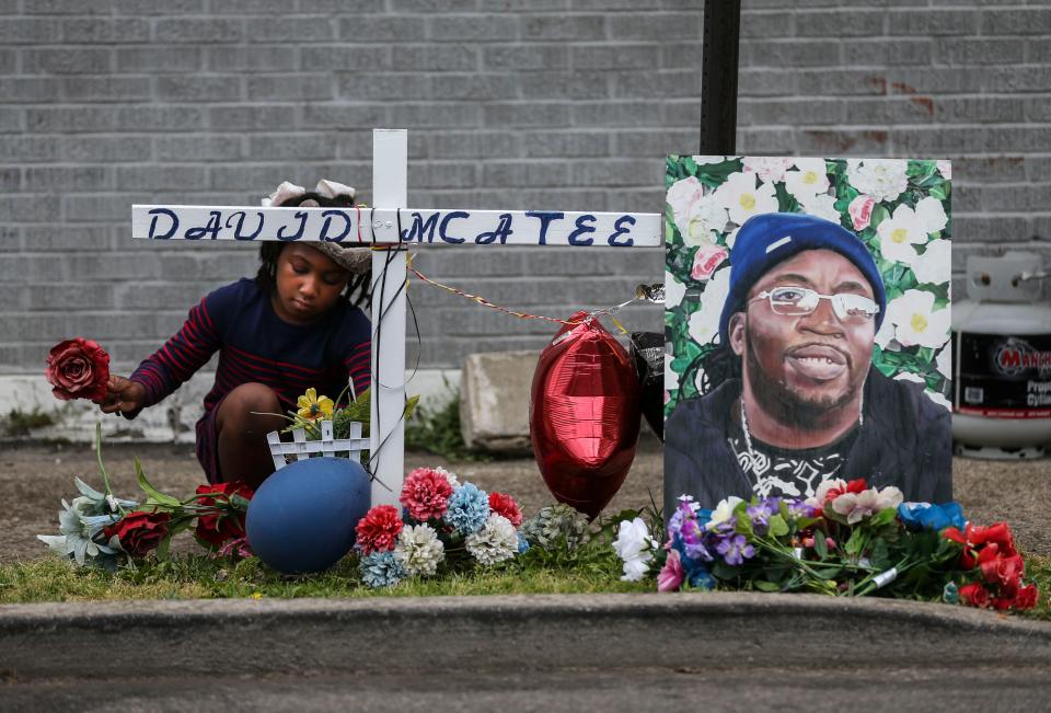 Nevaeh O'Bannon helps organize the flowers at a cross as a large photo of David 'YaYa' McAtee leans against a street post during a memorial after a balloon release outside of the former YaYa's BBQ in 2021.