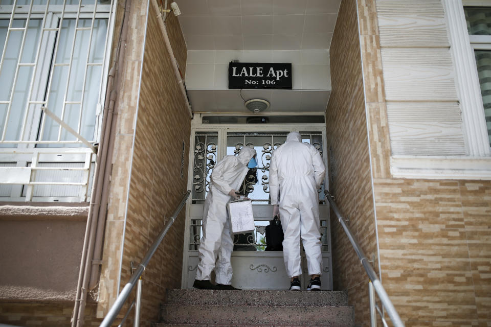 In this Friday, May 15, 2020 photo, contact tracers with Turkey's Health Ministry's coronavirus contact tracing team, clad in white protective gear, masks and face shields, arrive at the house in Istanbul of Betul Sahbas, who had been experiencing COVID-19 symptoms, to take a sample. Teams of contact tracers in Istanbul, the epicenter of the pandemic in Turkey and its most populous city, and also nationwide, are going house to house to test people experiencing COVID-19 symptoms and inform patients on isolation. (AP Photo/Emrah Gurel)