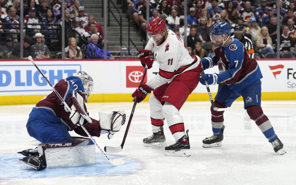 Colorado Avalanche goaltender Alexandar Georgiev, left, makes a glove save of a shot off the stick of Carolina Hurricanes center Jordan Staal (11) after he slipped past Colorado defenseman Devon Toews (7) in the second period of an NHL hockey game on Saturday, Oct. 21, 2023, in Denver. (AP Photo/David Zalubowski)
