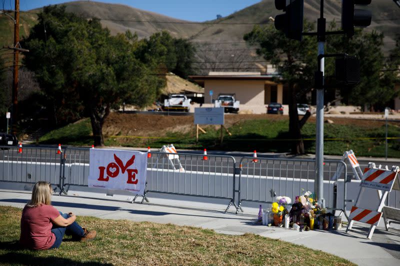 Jennifer Cassity, of Huntington Beach, sits on the ground after leaving flowers in memory of crash victim Christina Mauser at a makeshift memorial across from the helicopter crash site of NBA star Kobe Bryant in Calabasas