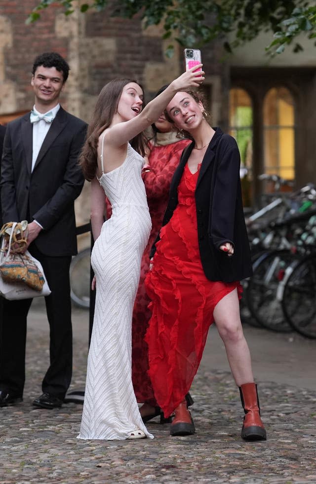 Two students take a selfie as another watches 