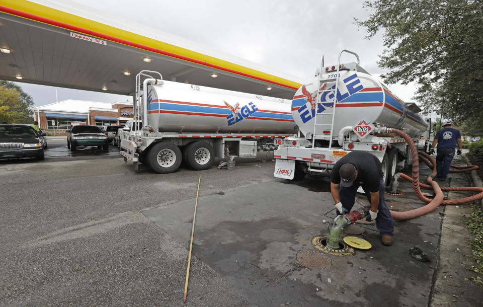 FILE- In this Sept. 17, 2018, file photo people wait in line as Travis Hall, right, and Brandon Deese, back, pump fuel from two tanker trucks at a convenience store in Wilmington, N.C. America's rediscovered prowess in oil production is shaking up old notions about the impact of higher crude prices on the U.S. economy. (AP Photo/Chuck Burton, File)