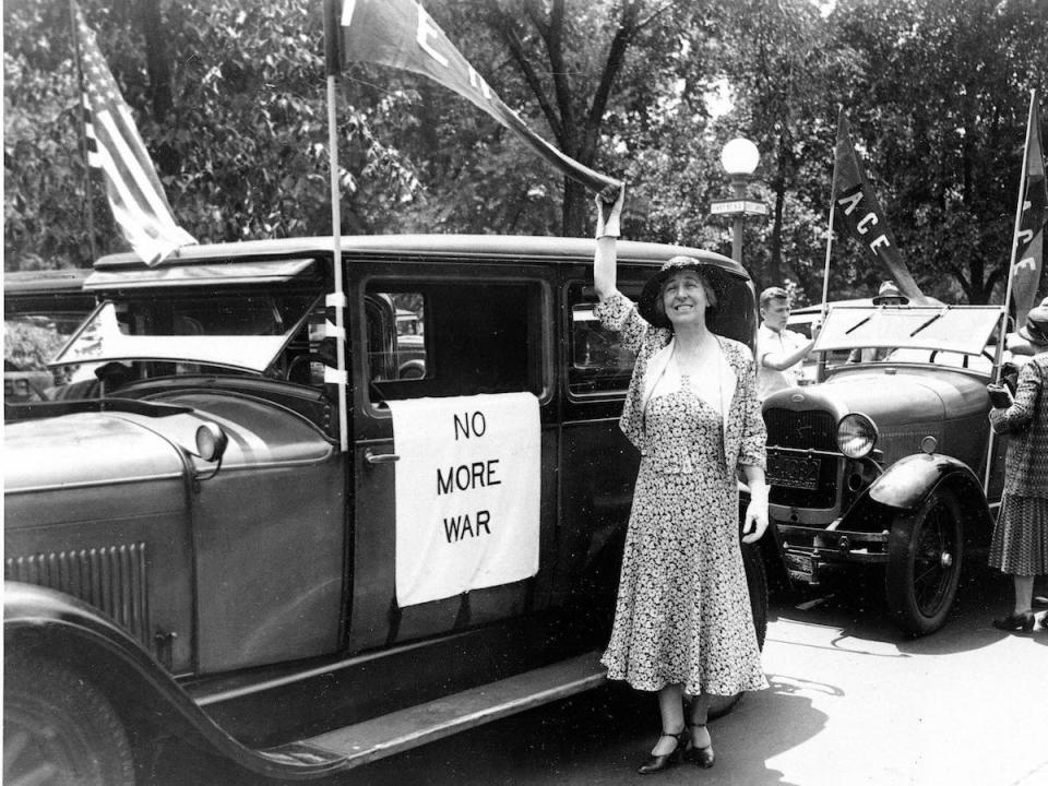 Jeannette Rankin stands next to a car with a sign that says "No more war."