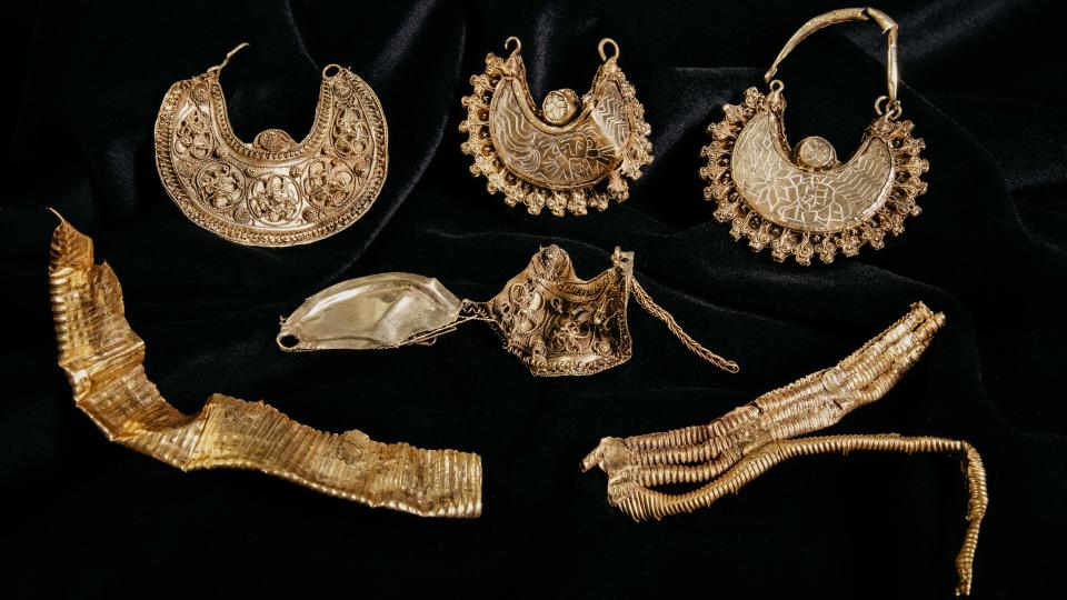 Intricate golden jewelry is displayed on black velvet.