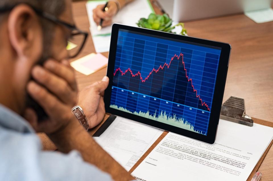 A visibly worried person looking at a stock chart that rises rapidly and then falls, displayed on a tablet.