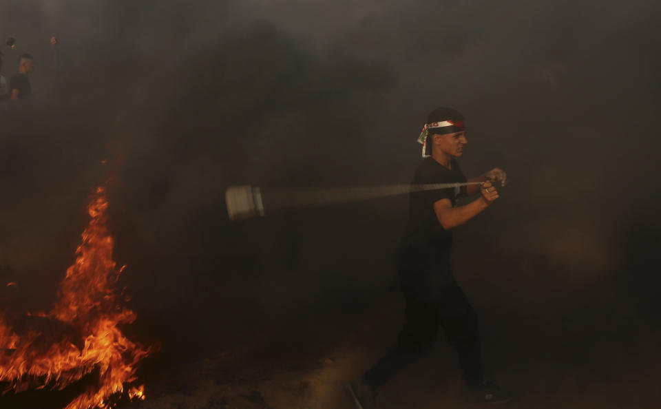 A protester hurls stones at Israeli troops while others burn tires near the fence of the Gaza Strip border with Israel, during a protest east of Khan Younis, southern Gaza Strip, Friday, Oct. 5, 2018. Israeli forces shot dead three Palestinians, including a 13-year-old boy, as thousands of people protested Friday along the fence dividing the Gaza Strip and Israel, Gaza's Health Ministry said. (AP Photo/Adel Hana)