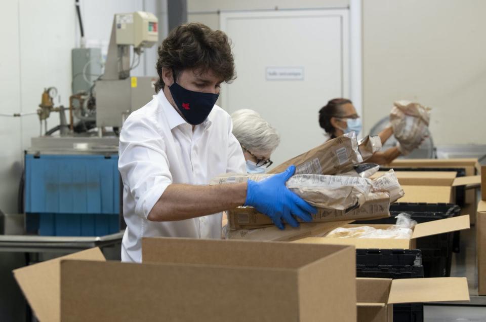 Justin Trudeau, wearing a mask and gloves, places items in a cardboard box.