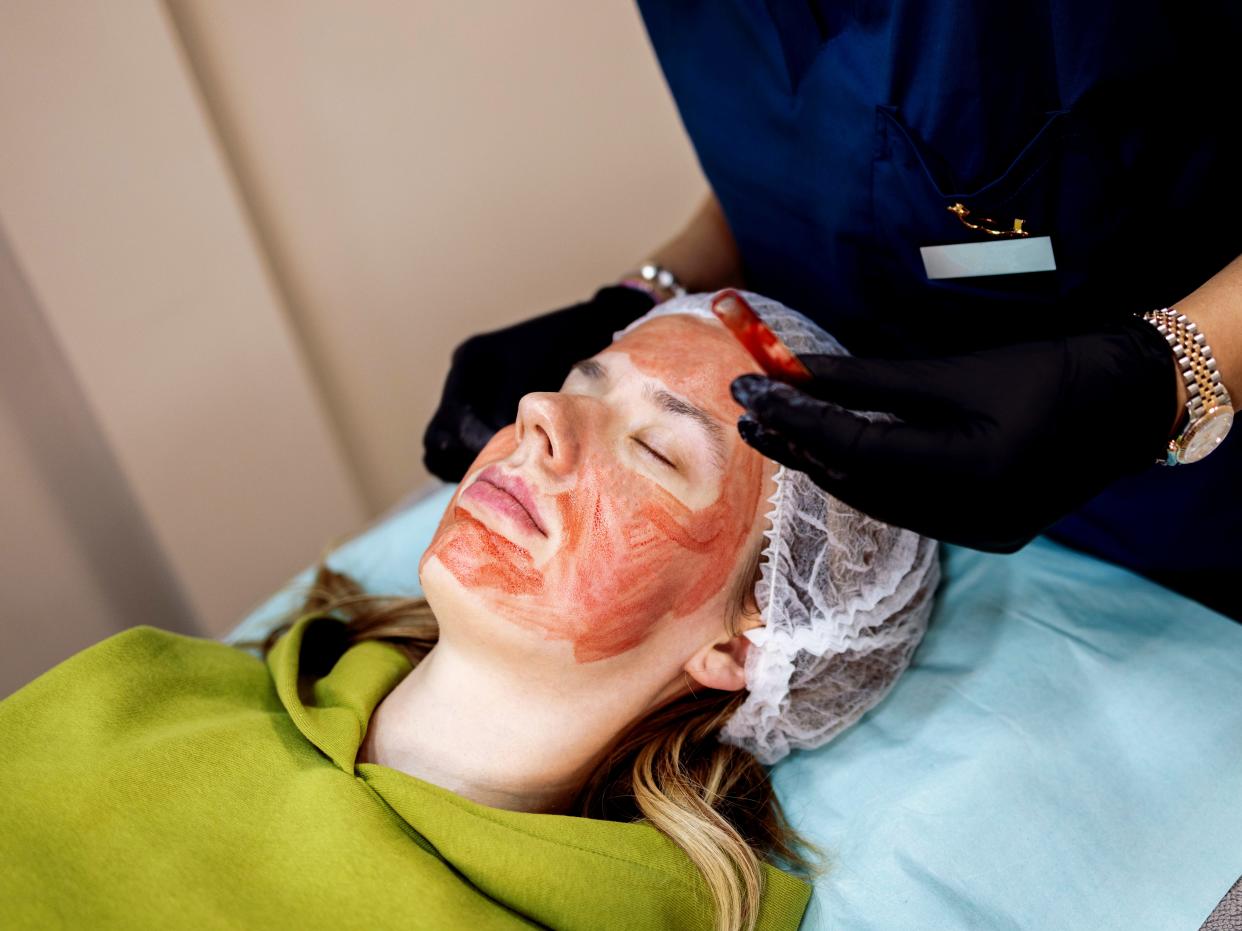 Woman lying on medical table with blood on her face, a doctor is standing behind her in blue scrubs.