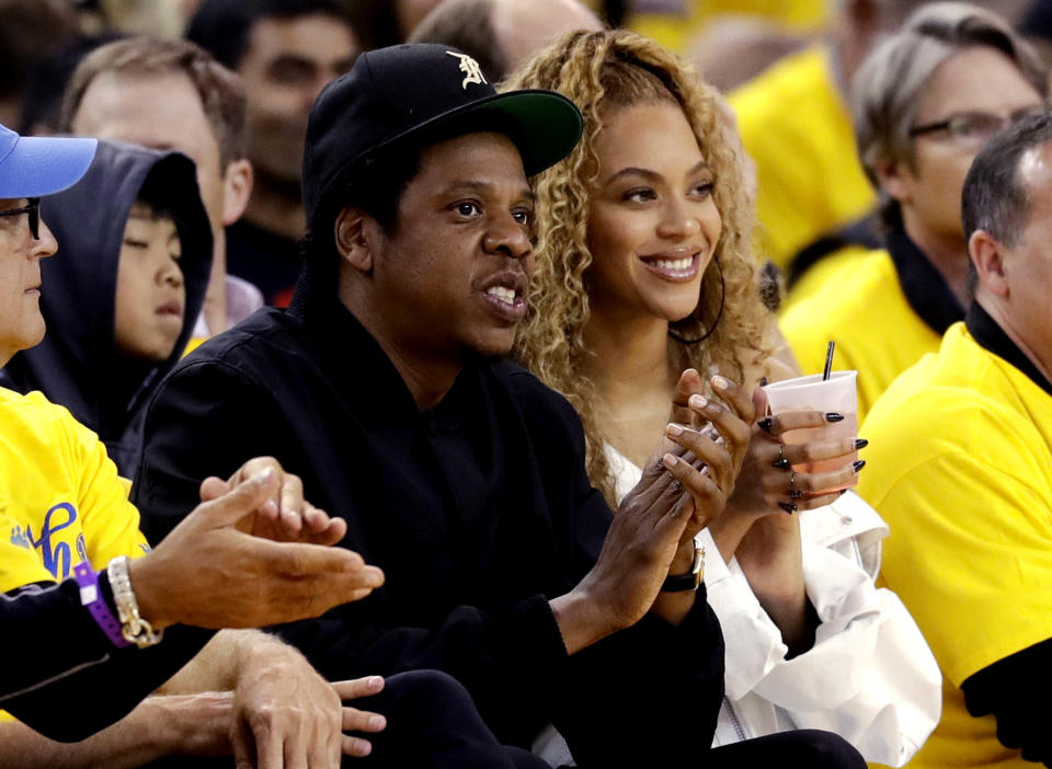 FILE - In this April 28, 2018, file photo, Jay-Z and Beyonce watch Game 1 of an NBA basketball second-round playoff series between the Golden State Warriors and the New Orleans Pelicans in Oakland, Calif. Just as a movie soundtrack helps viewers follow the action of the narrative through each plot twist, hip-hop has done the same for basketball via the NBA. It underscores how hip-hop has used the NBA to step outside its urban origins and reach every corner of the country. Once derided by mainstream America, the words and contributions of hip-hop artists now impact the masses. Jay-Z not only bought a minority a stake in the Brooklyn Nets but designed the uniforms. (AP Photo/Marcio Jose Sanchez, File)