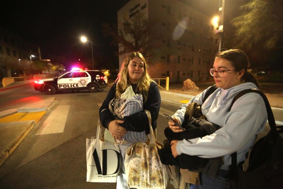 Two young woman stand holding bags.