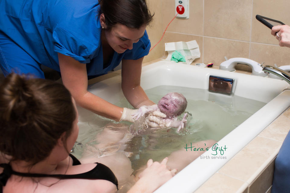 "After a quick second labor for this mom, her midwife lifts her baby out of the birth tub with her husband and mom looking on."