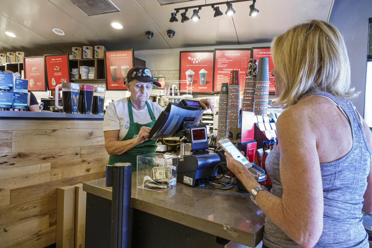 Florida, Palm Beach Gardens, Starbucks Coffee, mature adult barista with customer, who is using mobile payment on smart phone. (Photo by: Jeff Greenberg/Education Images/Universal Images Group via Getty Images)