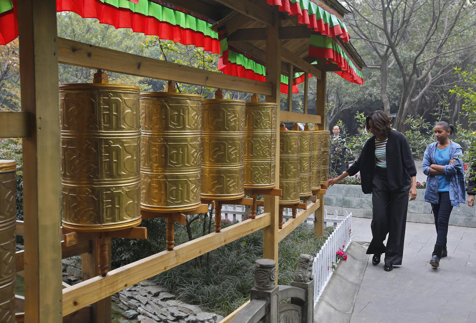 U.S. first lady Michelle Obama, left, touches Tibetan prayer wheels as her daughter Sasha watches outside a Tibetan restaurant in Chengdu, Sichuan province, China Wednesday, March 26, 2014. (AP Photo/Petar Kujundzic, Pool)