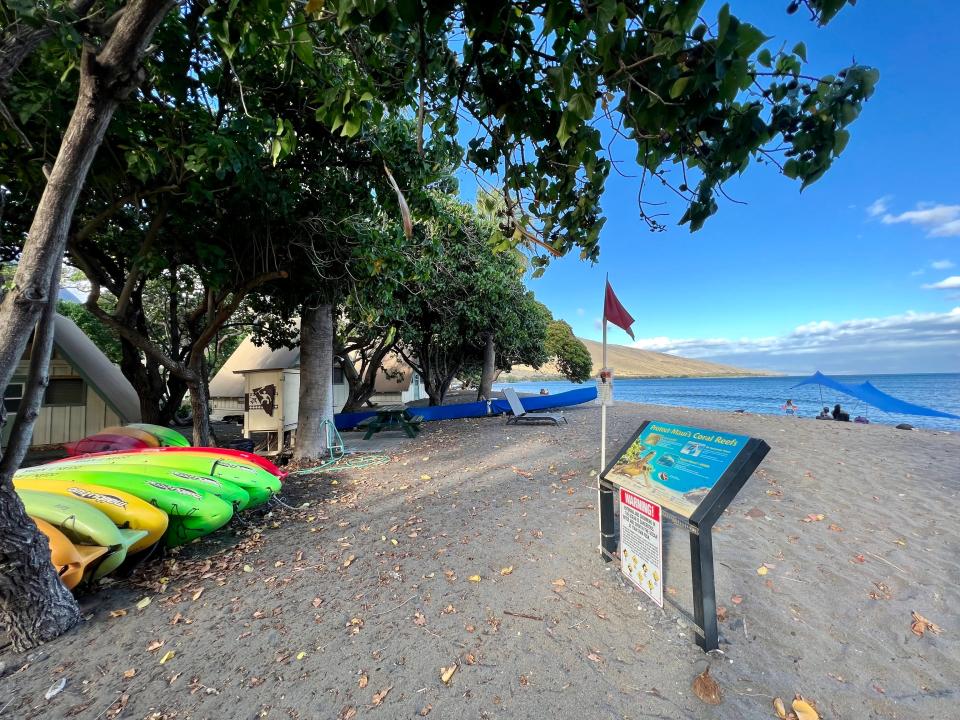 a beach with kayaks on it and a small sign board and blue skies