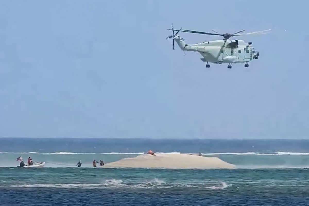 This frame grab from video footage taken and released on 25 March 2024 by the Philippine Bureau of Fisheries and Aquatic Resources (PCG/BFAR) shows a Chinese helicopter hovering as Philippine scientists inspect a cay near the Philippine-held Thitu Island, in the Spratly Islands, in the disputed South China Sea (Philippine Coast Guard/AFP via G)