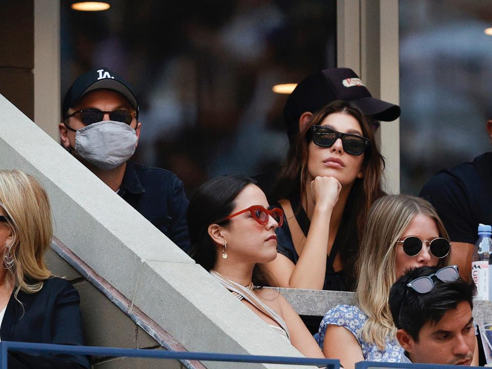 Leonardo DiCaprio, in a gray mask and baseball cap, and Camila Morrone, in dark sunglasses, watch a tennis match during the 2021 US Open.